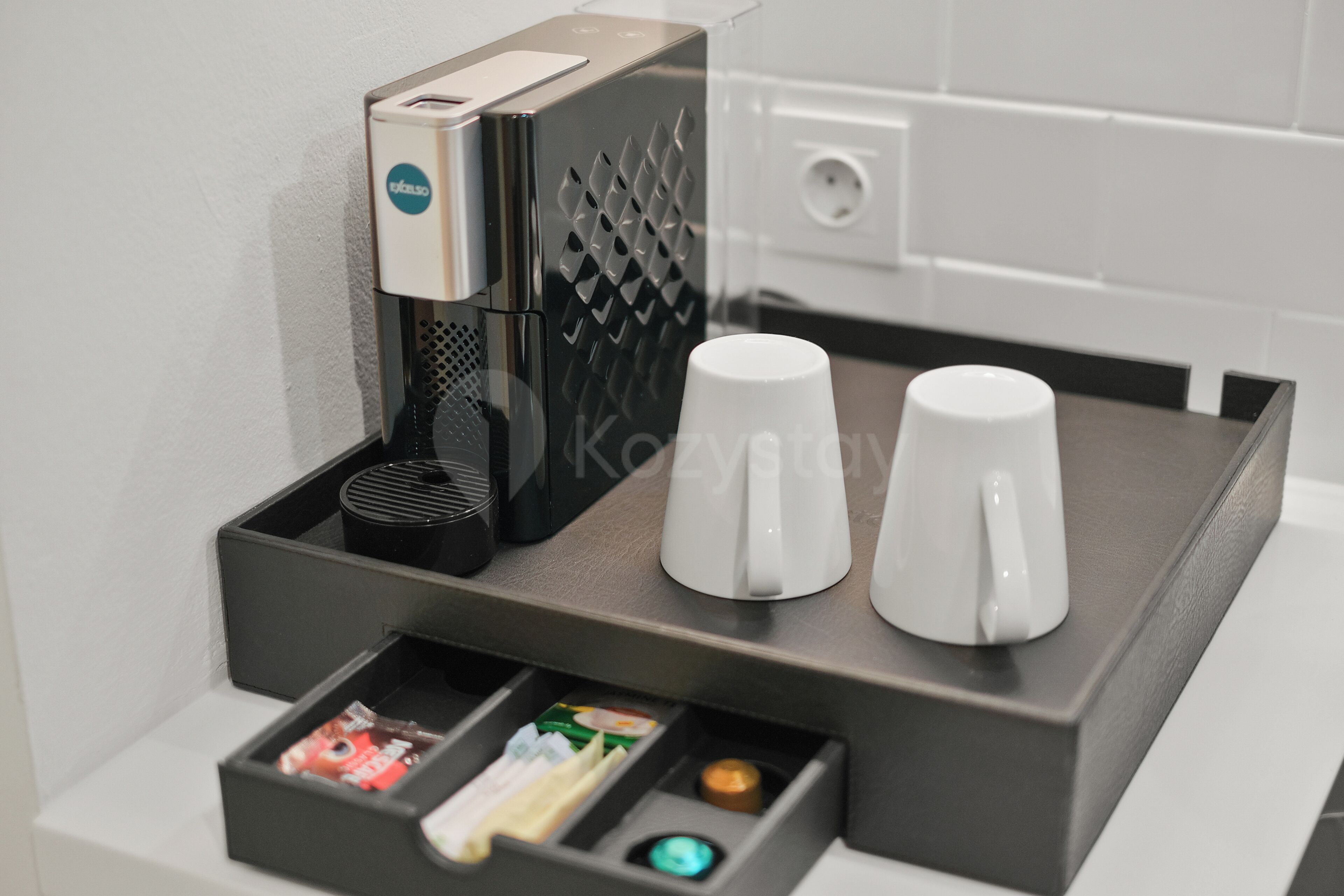 A coffee machine with two white cups and a tray with various coffee pods.