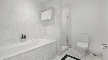 A bathroom with a bathtub, shower, toilet, and marble walls.