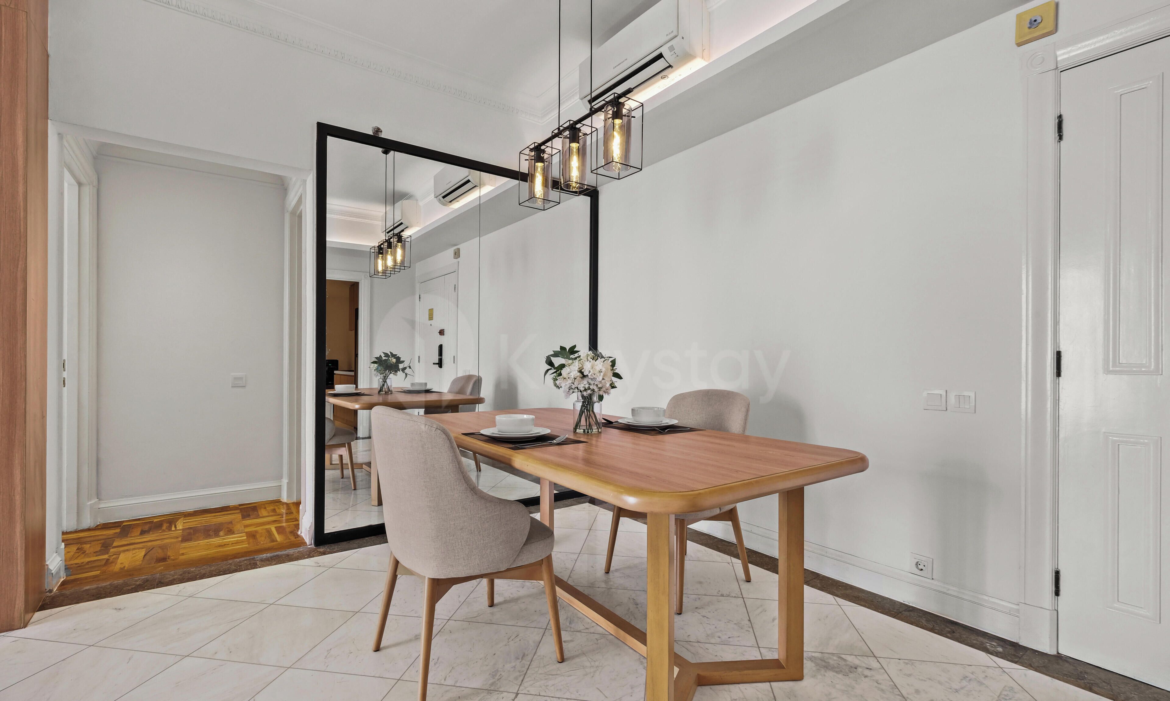 Un comedor con mesa de madera, sillas y una lámpara colgante moderna.
