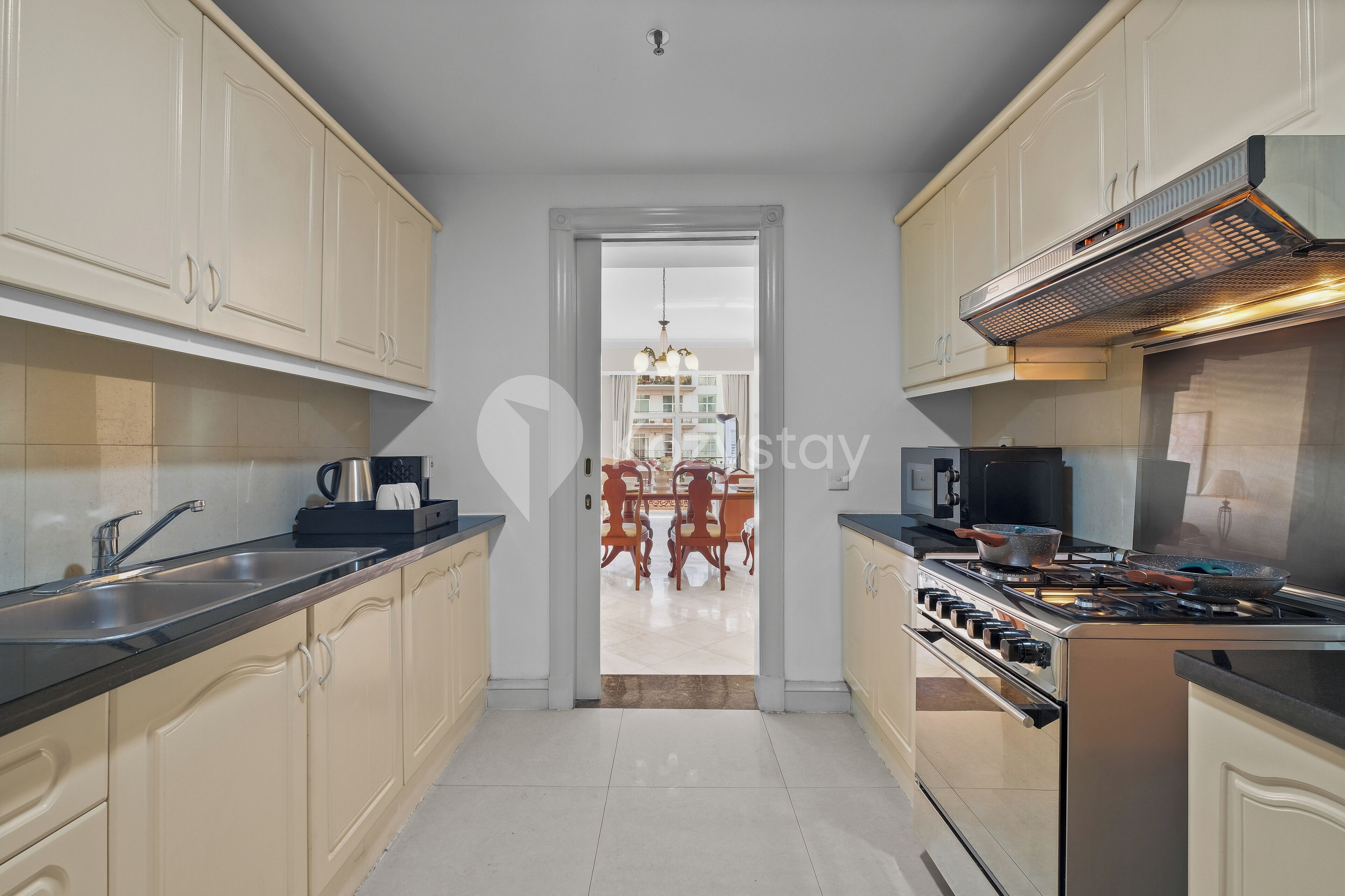 Una cucina moderna con mobili beige, un piano di lavoro nero, elettrodomestici in acciaio inox e vista su un'area pranzo con un lampadario.