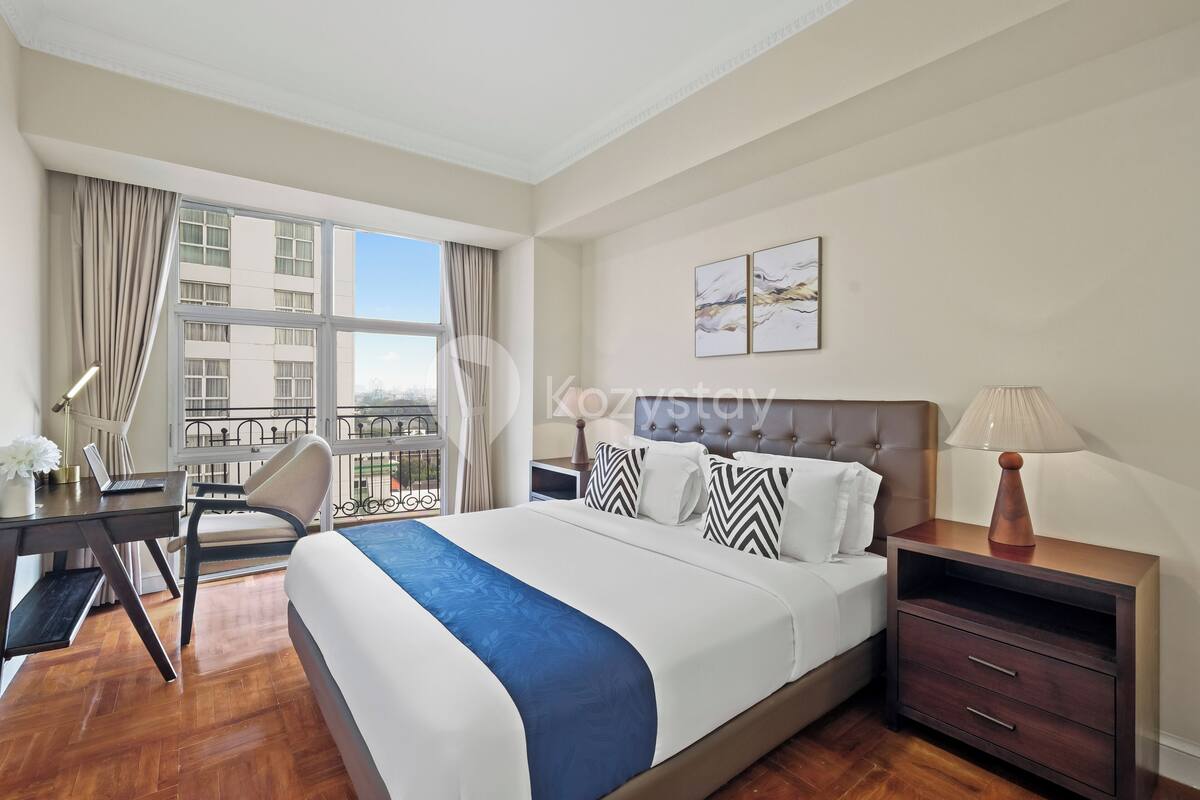 Une chambre d’hôtel avec un grand lit, un bureau, une chaise, une table de chevet et une fenêtre avec des rideaux.