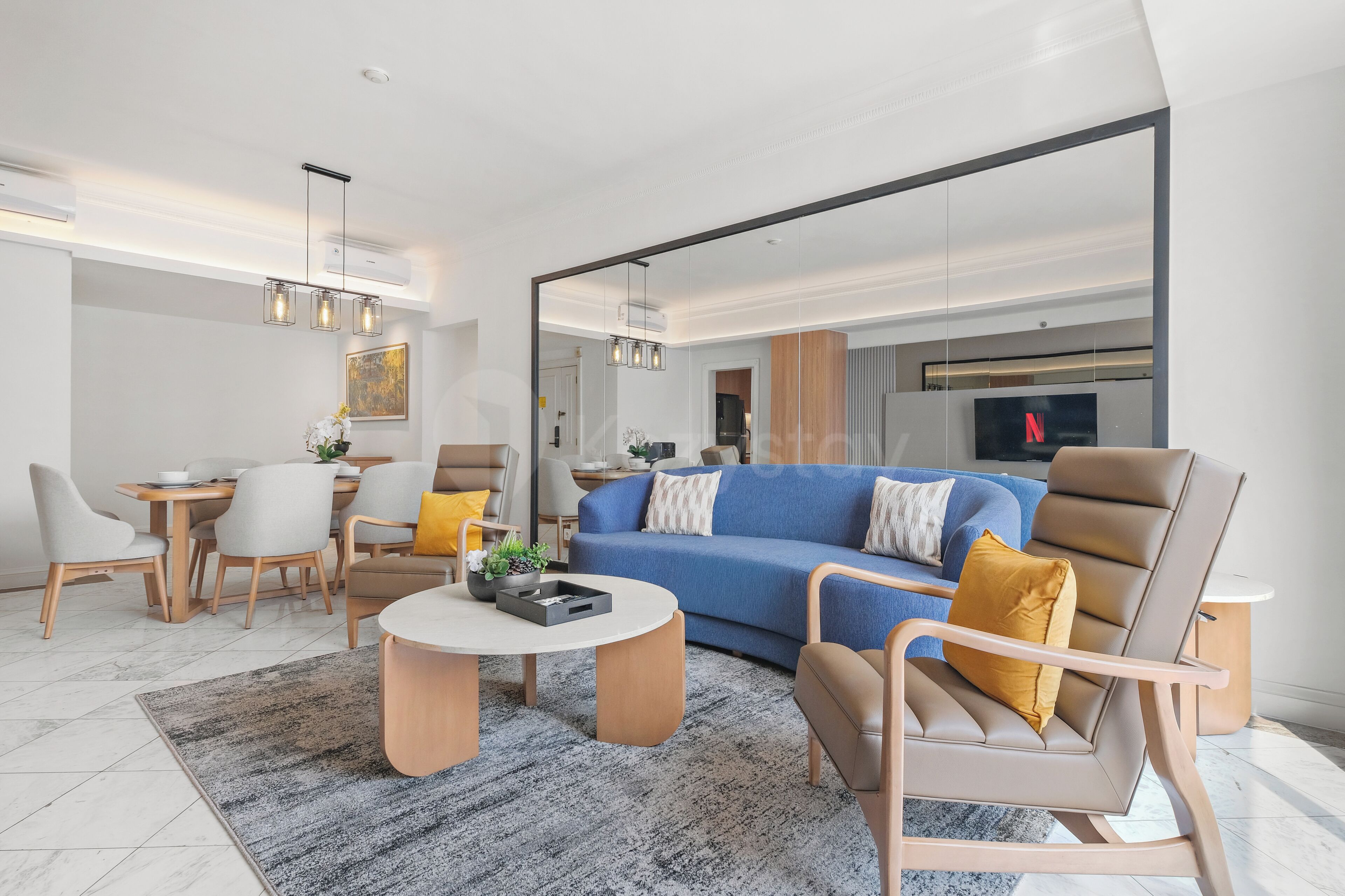 A modern living room with a blue sofa, a brown armchair, a dining table with chairs, and a coffee table.