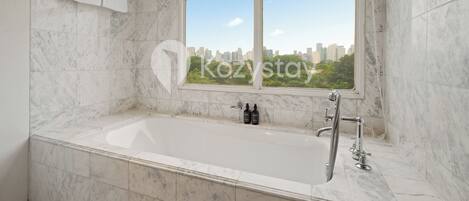 A modern bathroom with a large bathtub, a window with a city view, and marble tiles.