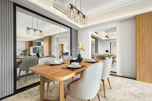 A modern dining area with a wooden table, grey upholstered chairs, and pendant lighting. - Rasamala & Cendana at Menteng by Kozystay (Jakarta)