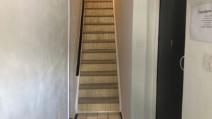 A narrow staircase with wooden steps and a handrail, leading to a door with a fire alarm sign. - Stylish flat in Chesterfield near Peak District (Chesterfield)