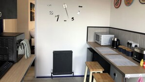 A kitchen with a wall clock, a microwave, a kettle, and a small table. - Stylish flat in Chesterfield near Peak District (Chesterfield)