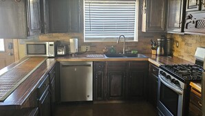 A kitchen with dark wooden cabinets, a stainless steel sink, a built-in oven, and a window with blinds.
