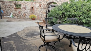 An outdoor patio area with a stone wall, a round table with chairs, and a potted plant.