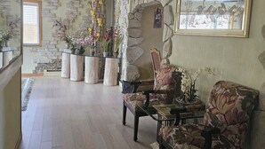 A spacious living room with a stone wall, a large framed painting, and a variety of potted plants.