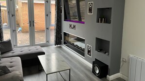 A modern living room with a grey sofa, a marble coffee table, and a built-in entertainment unit with speakers and shelves.