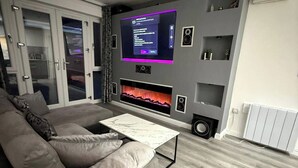 A modern living room with a grey sofa, a marble coffee table, a fireplace, and a wall-mounted entertainment unit with speakers.