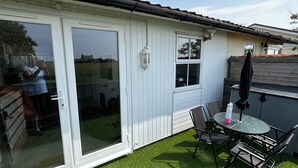 A patio with artificial grass, a table with chairs, and a sliding glass door. - Seaside Chalet Escape in Bridlington (Bridlington)
