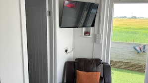 A room with a leather chair, a mounted TV, and a view of a green field through a window. - Seaside Chalet Escape in Bridlington (Bridlington)