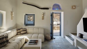 A modern living room with a sectional sofa, a small table, a view of a village through a door, and a ceiling fan.