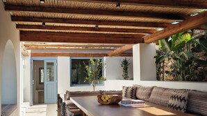 A dining area with a wooden table, chairs, and a bench. There is a window with a view of the outside, and a door leading to another room.