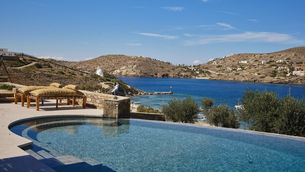 A clear blue sky, a swimming pool with a stone edge, and a view of a coastal landscape with buildings.