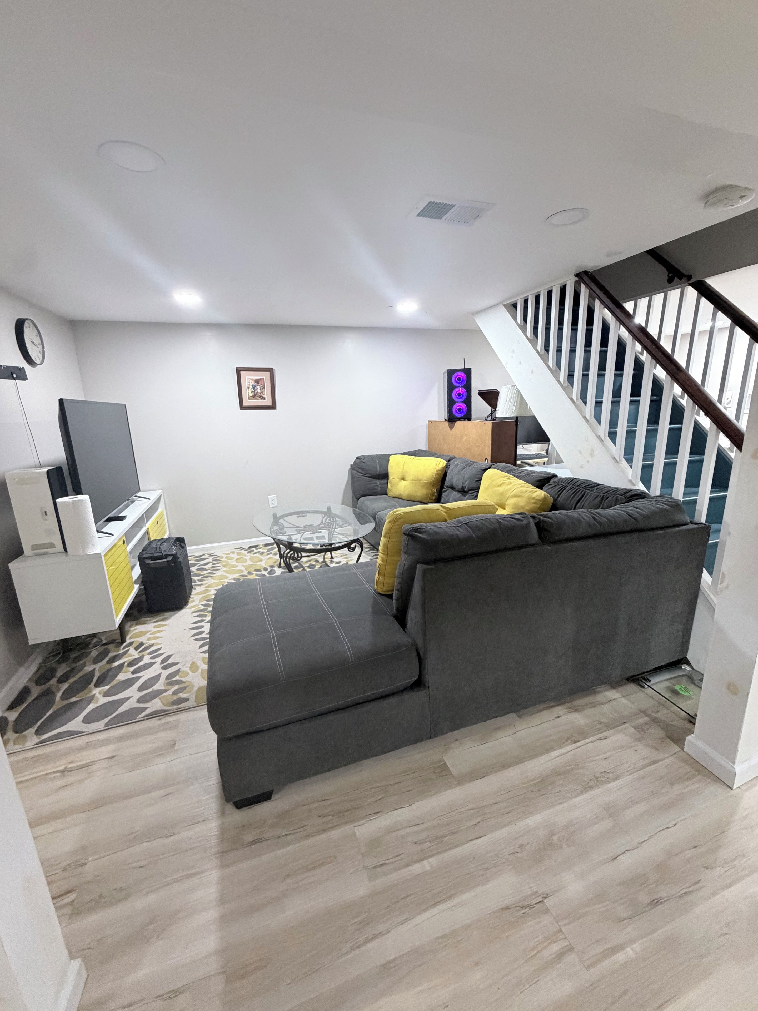 A modern living room with a grey sofa, a glass coffee table, and a staircase with white railings.