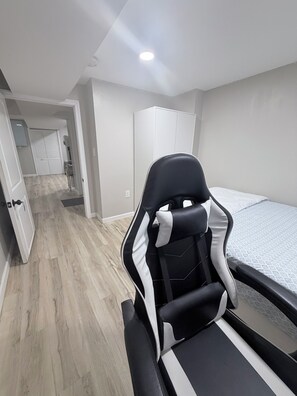 A room with a bed, a chair, a wardrobe, and a door leading to another room.