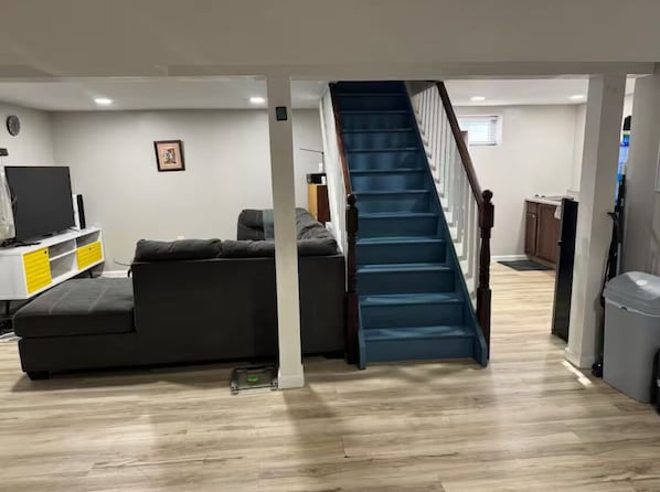 A living room with a grey sofa, a TV, and a staircase leading to another room.