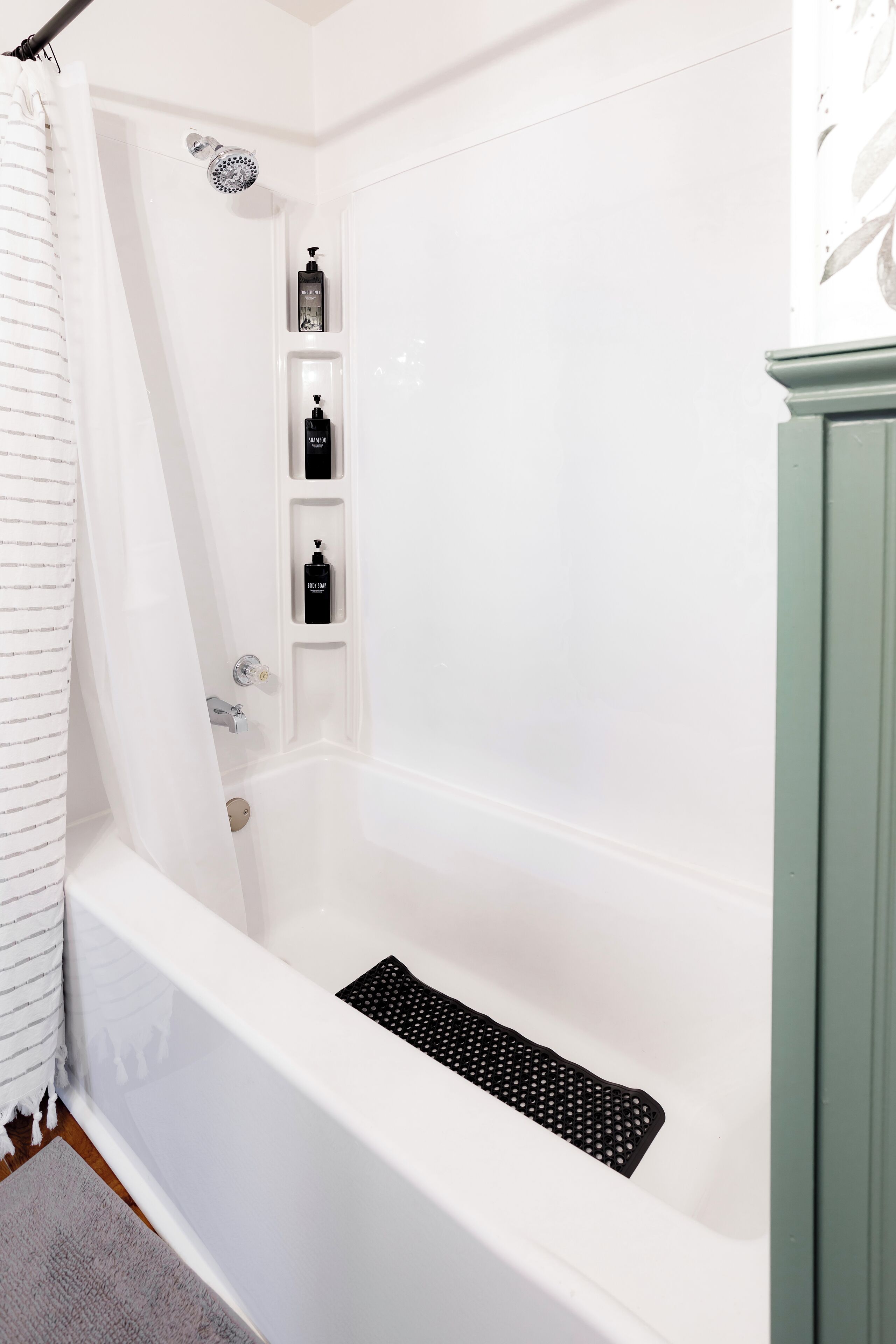 A white bathtub with a showerhead, a black drain, and three black bottles on a shelf.