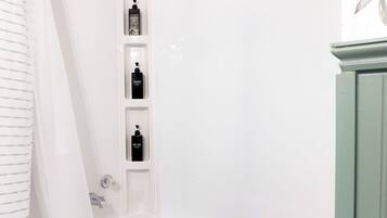 A white bathtub with a showerhead, a black drain, and three black bottles on a shelf.