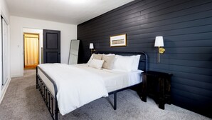 A bedroom with a bed, a dark wall, a framed picture, and two wall-mounted lamps. - King Size Bed, Near Hwy, Work Desk, Parking Just A Few Feet Away (Lockport)