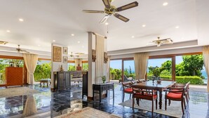 A spacious room with a dining area, a kitchen, and large windows offering a view of the outdoors. - Baan Phuttarak Villa - 4BR Private Sea View (Ko Samui)