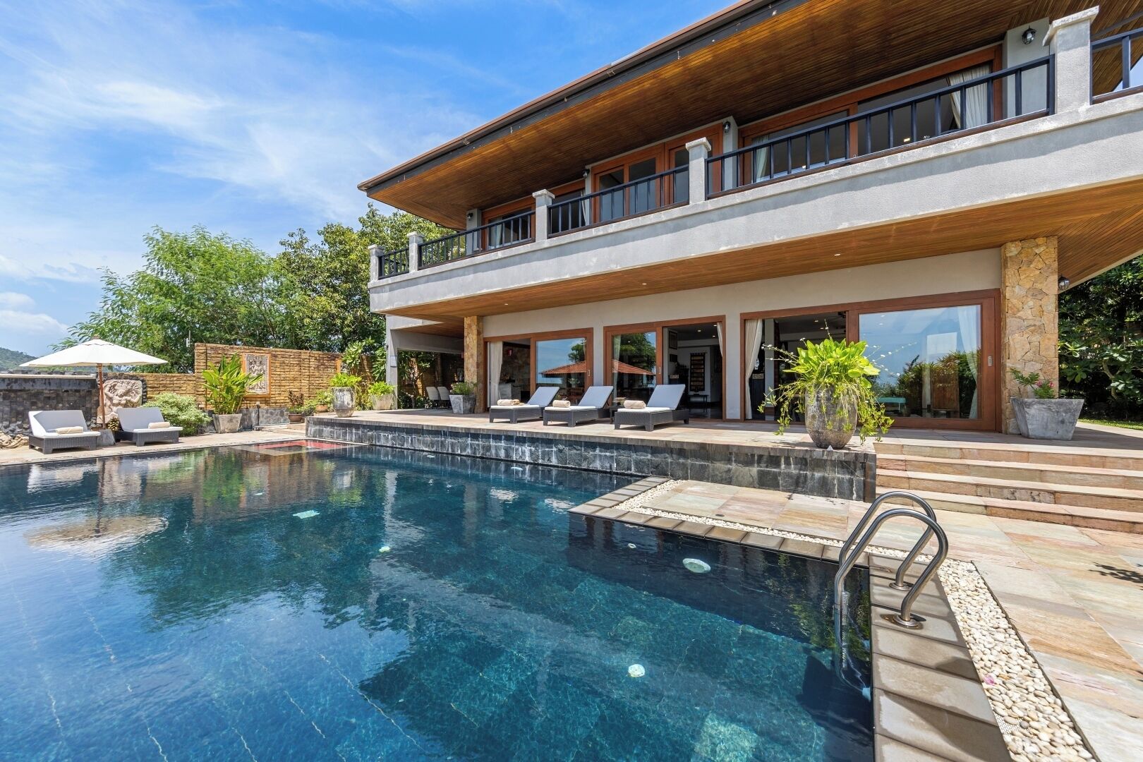 Una casa moderna con piscina, mobiliario de exterior y fachada de piedra.