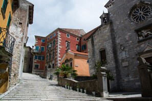 Una calle estrecha con una escalera de piedra que conduce a un edificio de fachada roja y una torre con reloj.