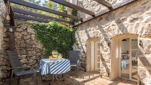 A stone-walled patio with a table and chairs, a stone wall with greenery, and an arched doorway. - La Rocca Duo - Hidden In Istria, Labin, Croatia (Labin)