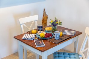 A breakfast table with a book, a glass of orange juice, a plate with berries, a mug, and a vase with flowers.