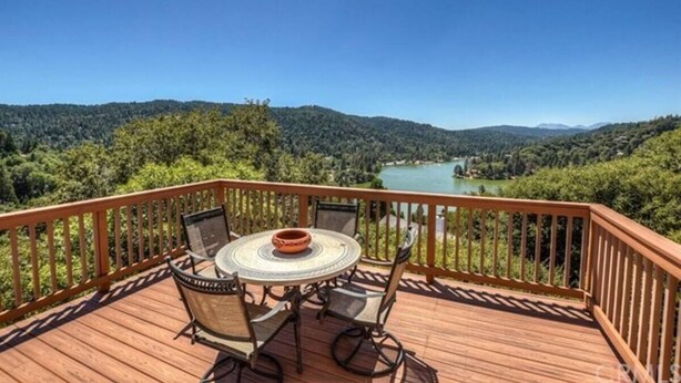 A wooden deck with a round table and chairs, overlooking a lake and forested hills.