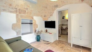 A living room with a stone wall, a flat-screen TV, a sofa, a cabinet, and a bathroom visible in the background.