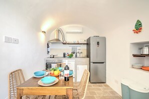 A compact kitchen with a dining table, chairs, a refrigerator, and a wall-mounted shelf. - Dimora Tra Gli Ulivi With Private Jacuzzi, Ostuni, Italy (Ostuni)