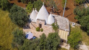 A stone building with three conical roofs, surrounded by trees and a small stream.