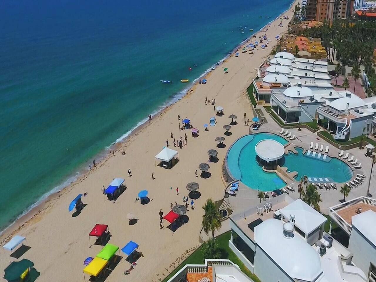 An aerial view of a beach resort with a large pool, beach umbrellas, and beach chairs.