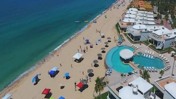 An aerial view of a beach resort with a large pool, beach umbrellas, and beach chairs.