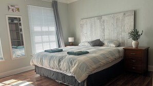 Une chambre à coucher bien rangée, avec un grand lit, une table de chevet, une commode, une fenêtre avec des stores et une armoire.