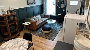 Un salon chaleureux avec un canapé marron, une table en marbre et une petite table ronde. On y trouve une bibliothèque, un crâne décoratif et un lustre.
