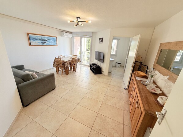 A spacious living area with a sofa, dining table, chairs, and a TV.