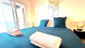 A neatly made bed with a blue textured bedspread, a folded white towel, and a blue pillow.