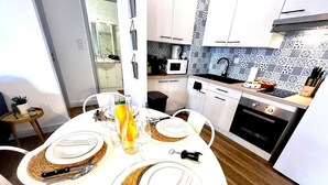 A modern kitchen with white cabinets, a microwave, and a coffee maker. There is a dining table set with plates, cutlery, and a bottle of water.