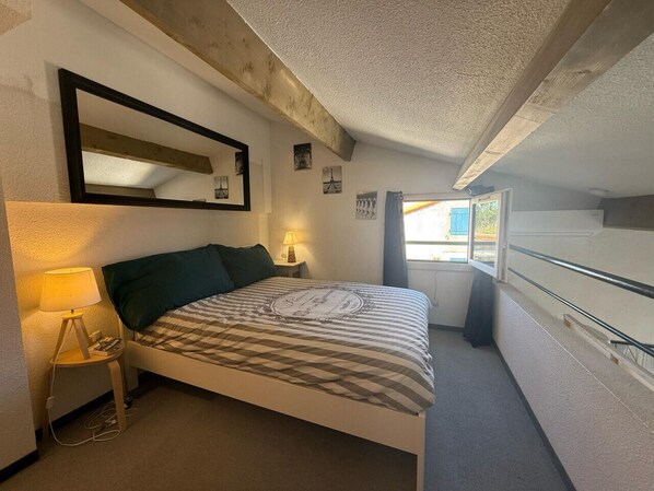 Ein Schlafzimmer mit Bett, Nachttisch, Lampe, Spiegel und Fenster.