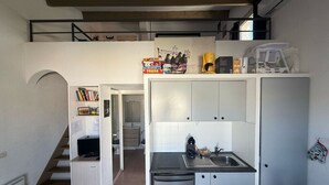 A compact kitchen with white cabinets, a sink, and a small refrigerator. There is a staircase leading to a second floor, and a bookshelf with various items on the left. - Côté Sud - Swimming pool, BBQ and CLIM (Vic-la-Gardiole)
