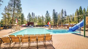 Une piscine avec des chaises longues, un toboggan et un petit bâtiment situé dans un espace boisé.