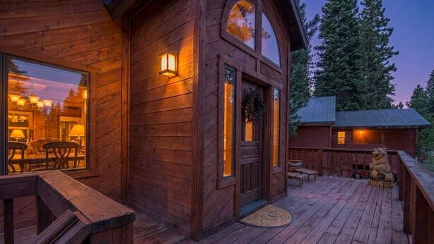 Une cabane en bois dotée d’une terrasse, de grandes fenêtres et d’une statue en pierre.