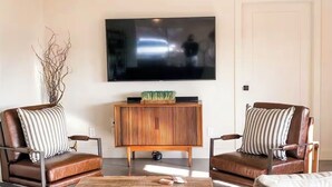 Ein Wohnzimmer mit zwei Ledersesseln, einem Holztisch und einem an der Wand befestigten Flachbildfernseher.