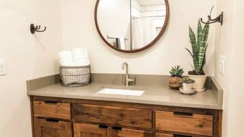Une salle de bain avec un meuble-lavabo en bois, un miroir rond, un évier et une plante en pot.
