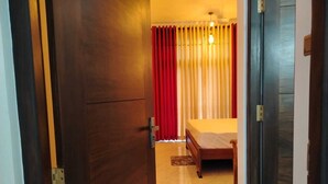 Un dormitorio con una cama, una puerta de madera y una ventana con cortinas rojas.