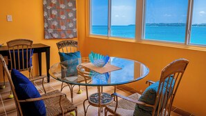 A dining area with a glass table and chairs, a view of the sea, and a wall with a coral pattern. - Condo by the sea (St. John's)